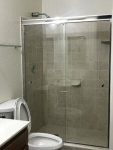 A clean shower with tiled walls and a glass door, next to a sparkling toilet, demonstrating A Clean Xscape LLC's house cleaning in Chandler, AZ.