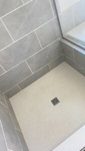 A sparkling clean shower floor with white hexagonal tiles and grey wall tiles, showcasing the results of cleaning by JLJ Sister's Cleaning & More in Lexington, KY.