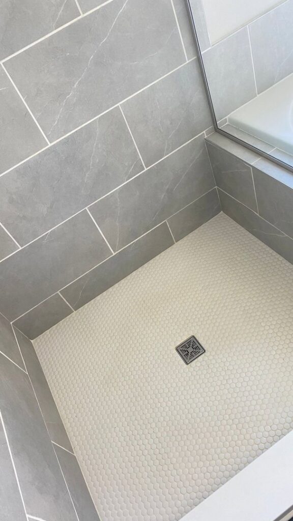 A sparkling clean shower floor with white hexagonal tiles and grey wall tiles, showcasing the results of cleaning by JLJ Sister's Cleaning & More in Lexington, KY.