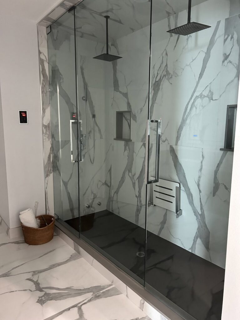 A clean and spacious glass shower enclosure with marble-patterned walls, expertly cleaned by JG Clean Solutions in Henderson, NV.