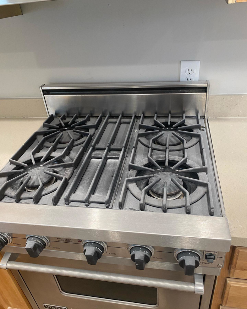 A close-up of a clean stainless steel stove top with grates, showcasing attention to detail by Hernanz Family Cleaning Services LLC in West Valley City, UT.