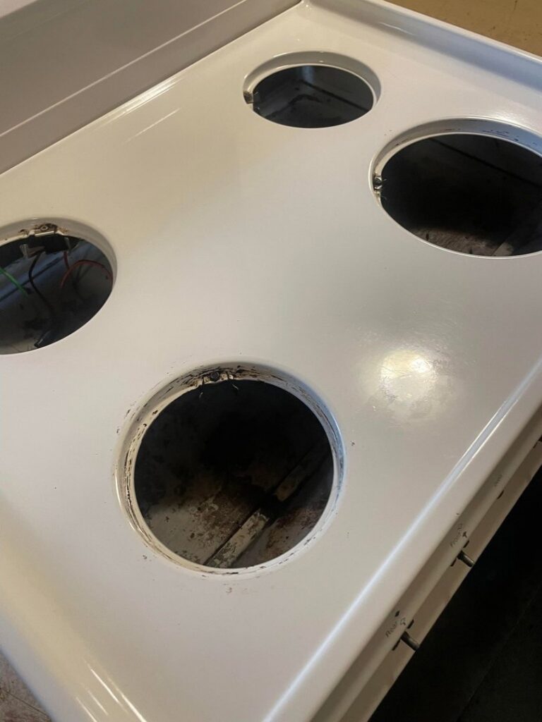 A sparkling clean white stove top with burners removed, showcasing deep cleaning by Skedaddle Cleaning Services in Eufaula, AL.