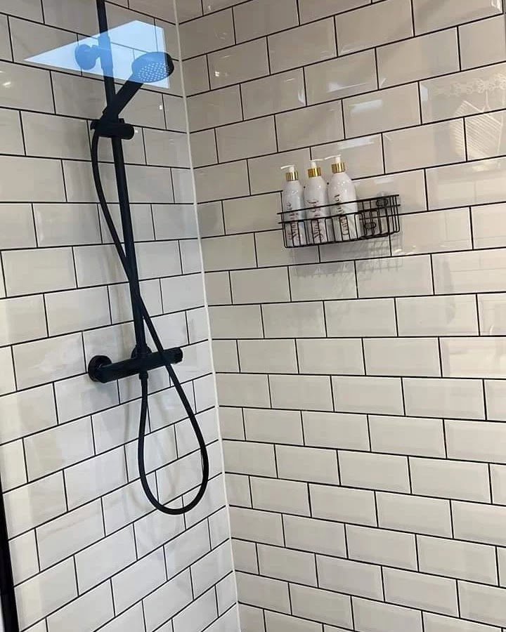 A pristine shower with white subway tiles and black fixtures, showcasing a professionally cleaned bathroom by Pretty & Polished Cleaning Services in Sandy, OR.