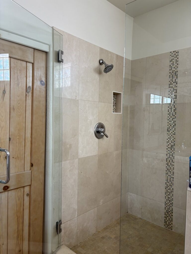 A sparkling clean shower with light-colored tiled walls and a clear glass door, maintained by Carole's House Cleaning in Tempe, AZ.