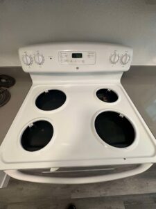 A clean white electric stove top with burner elements removed after professional cleaning by Nannie Needs LLC in Kent, WA.