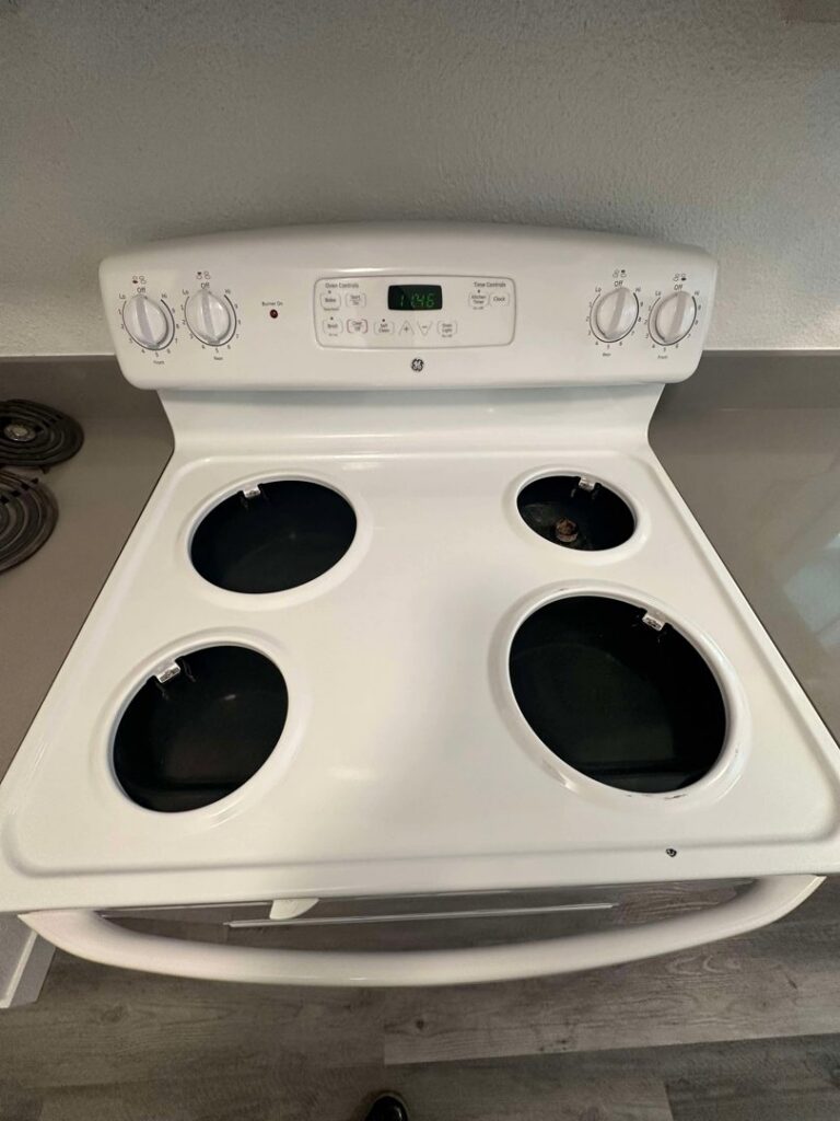 A clean white electric stove top with burner elements removed after professional cleaning by Nannie Needs LLC in Kent, WA.