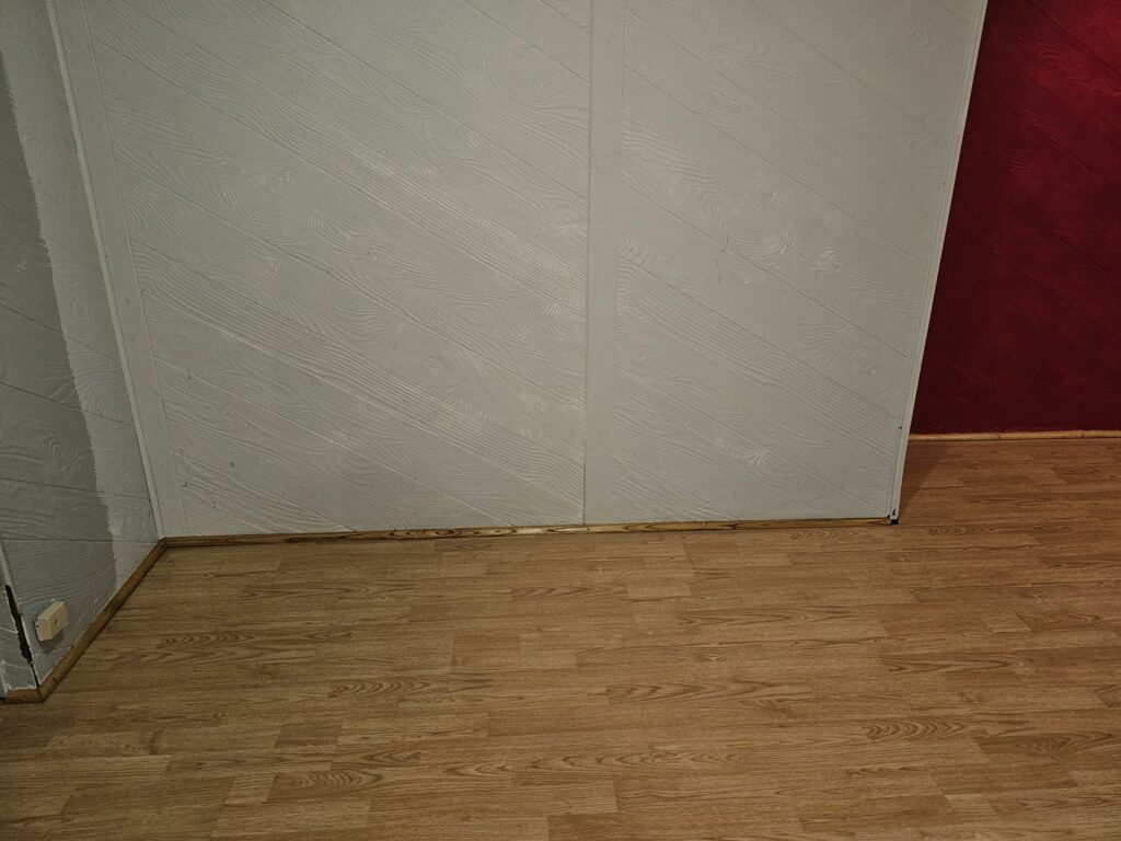 A close-up view of a clean wood-paneled wall and polished wood floor, showcasing attention to detail by Way Too Bright Services LLC in Rockford, IL.