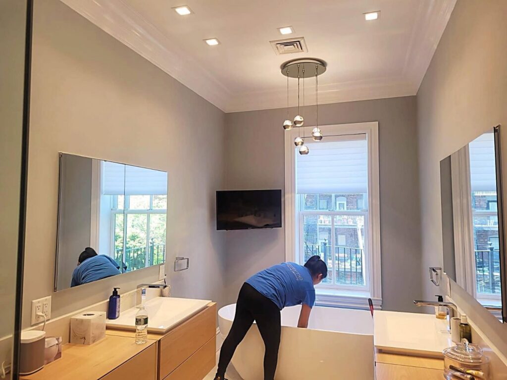 A professional cleaner from Supreme Home Cleaning, Inc cleaning a modern freestanding bathtub in Boston, MA.