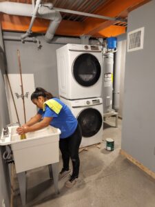 A house cleaner cleaning a utility sink in a laundry room with stacked washer and dryer units for Arizona Housekeeping Service in Phoenix, AZ.