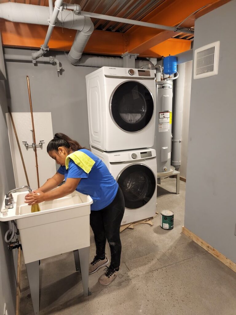 A house cleaner cleaning a utility sink in a laundry room with stacked washer and dryer units for Arizona Housekeeping Service in Phoenix, AZ.