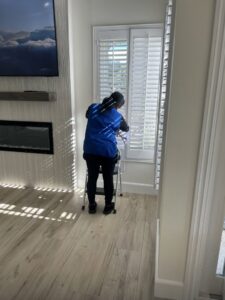 A cleaner from Fabylous Cleaning Service cleaning window blinds in a living room in Anaheim, CA.