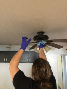 A cleaner wearing purple gloves dusting a ceiling fan, demonstrating house cleaning services by Alma's Cleaning Services in Sacramento, CA.