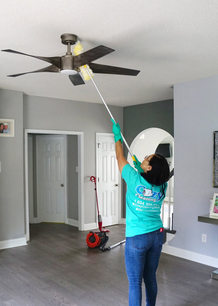 A professional cleaner from Cozy Cleaning VA dusting a ceiling fan with an extendable duster in a home in Richmond, VA.