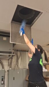 A cleaner from Absolute Luxury, LLC Residential & Commercial Cleaning uses a duster to clean a ceiling vent in Antioch, TN.