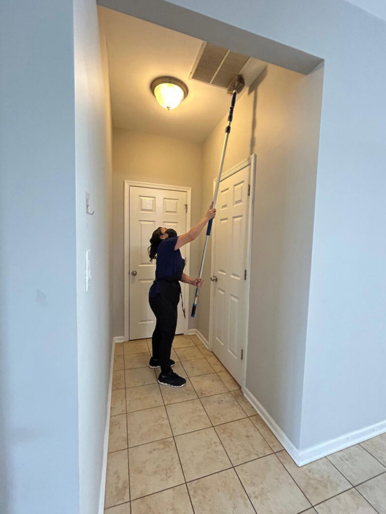 A professional cleaner from Bivian's Cleaners LLC dusting a ceiling vent in a hallway in Trenton, NJ.