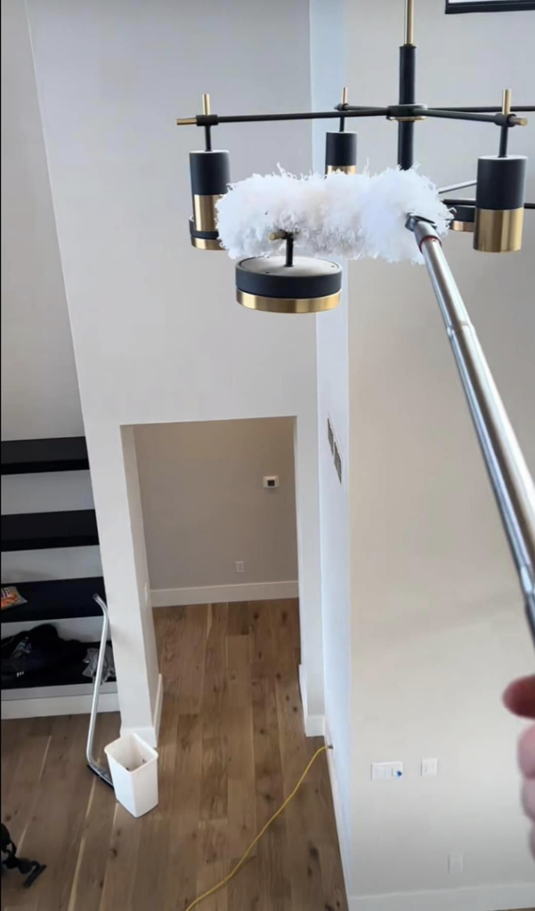 A professional cleaner using a long duster to clean a high chandelier for First Class Commercial and Residential Cleaning Services in Charlotte, NC.