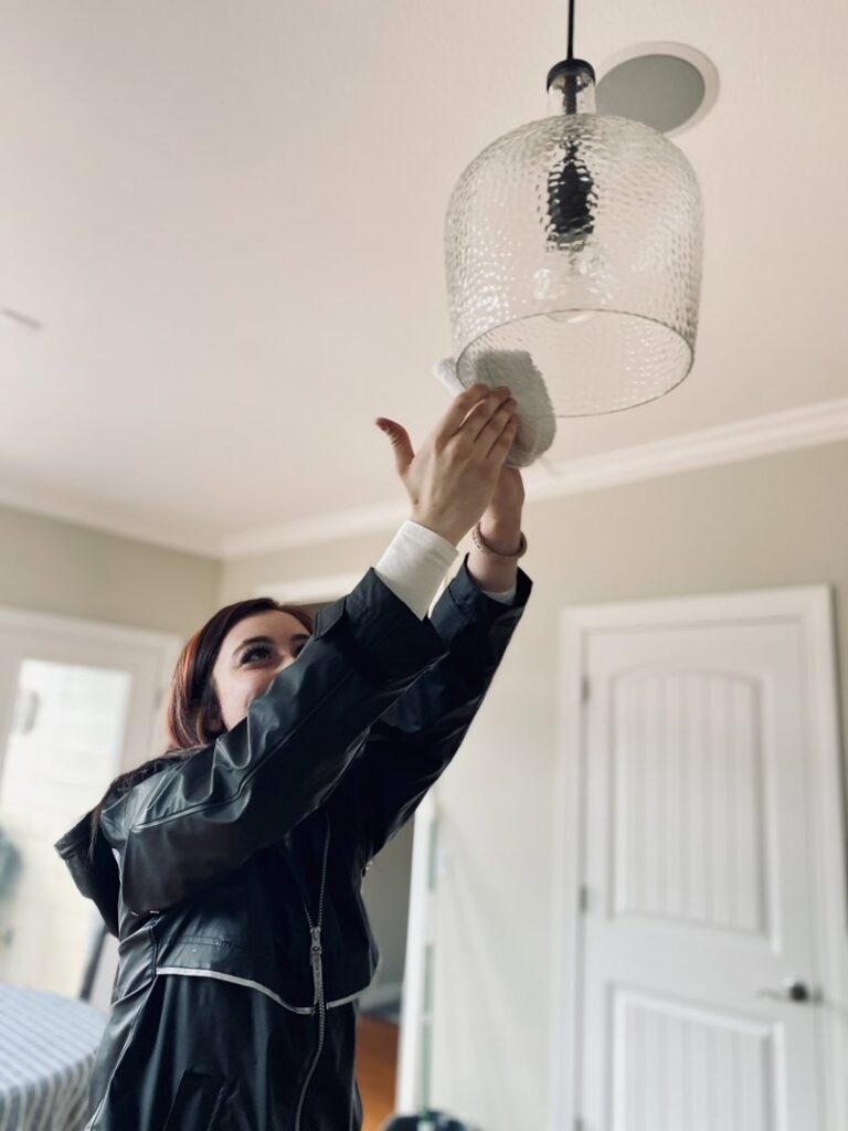 A professional cleaner dusting a light fixture, demonstrating attention to detail by Sudz Up Cleaning Company in Columbia, MO.