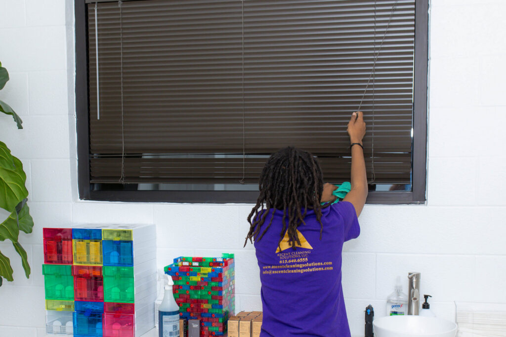 A house cleaner from Ascent Cleaning Solutions, LLC dusting window blinds in a home in Nashville, TN