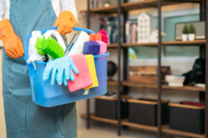 A house cleaner wearing an apron and orange gloves, holding a blue bucket of cleaning supplies for Clean Deeds in Olympia, WA.