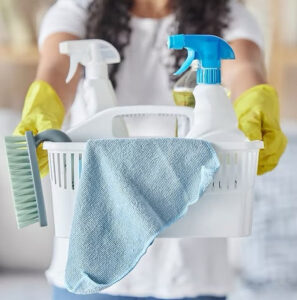 A house cleaner wearing yellow gloves holding a caddy filled with cleaning supplies for MAGA maids in Knoxville, TN.
