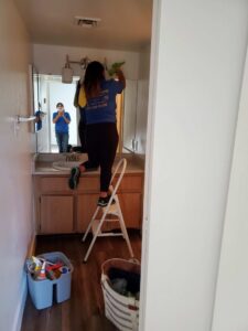 A house cleaner on a step ladder cleaning a bathroom mirror or cabinet for Arizona Housekeeping Service in Phoenix, AZ.