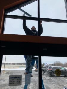A skilled cleaner on a ladder using a squeegee to wash a large window, a service from Blue Line Cleaning Services in Rock Hill, SC.
