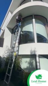 A professional cleaner on a ladder washing exterior windows for Leal Home Cleaning in San Francisco, CA.