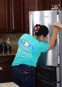 A professional cleaner from Cozy Cleaning VA polishing a stainless steel refrigerator in a kitchen in Richmond, VA.