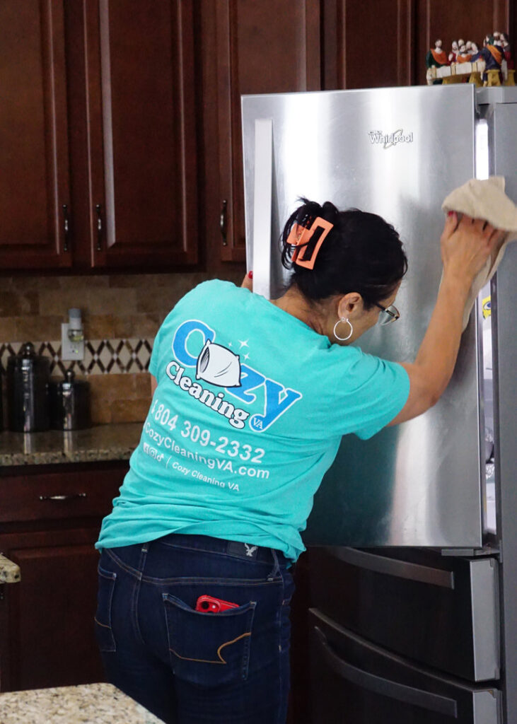 A professional cleaner from Cozy Cleaning VA polishing a stainless steel refrigerator in a kitchen in Richmond, VA.