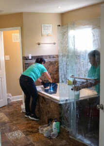 A professional cleaner from Cozy Cleaning VA scrubbing a bathtub and glass shower door in a bathroom in Richmond, VA.