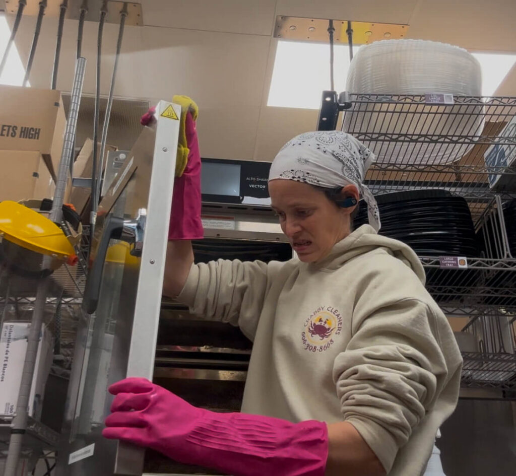 A professional cleaner wearing pink gloves scrubbing a metal surface in a commercial kitchen for Crabby Cleaners in Mount Vernon, KY