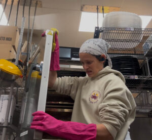 A professional cleaner wearing pink gloves scrubbing a metal surface in a commercial kitchen for Crabby Cleaners in Mount Vernon, KY