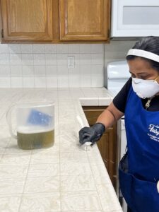 A cleaner from Fabylous Cleaning Service scrubbing a tiled kitchen countertop in Anaheim, CA.