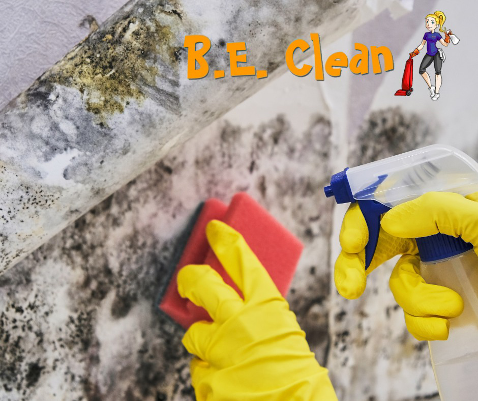 A house cleaner wearing yellow gloves sprays and scrubs a moldy wall, showcasing services by B.E. Clean in Toms River, NJ.
