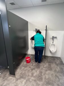 A cleaner from MJ Commercial & Residential Cleaning, LLC scrubbing a urinal in a commercial restroom in Cedar Rapids, IA.