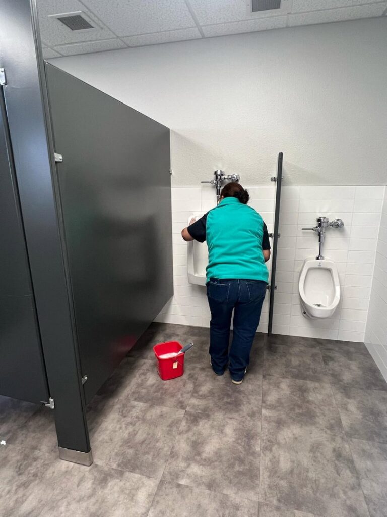 A cleaner from MJ Commercial & Residential Cleaning, LLC scrubbing a urinal in a commercial restroom in Cedar Rapids, IA.