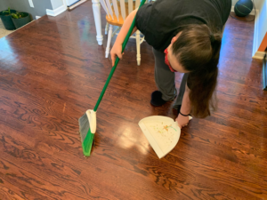 A cleaner from Bri and Sam's Cleaning Service sweeping a wooden floor with a broom and dustpan in Bonner Springs, KS.