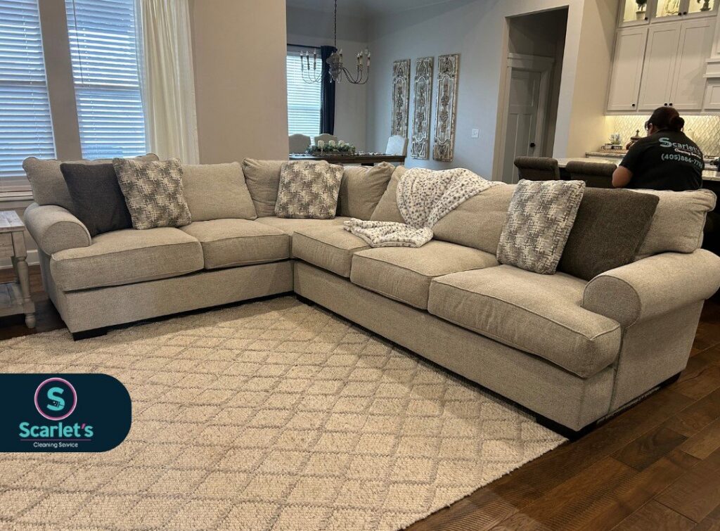 A cleaner tidying a living room with a large sectional sofa for Scarlet Cleaning Service LLC in Bronx, NY