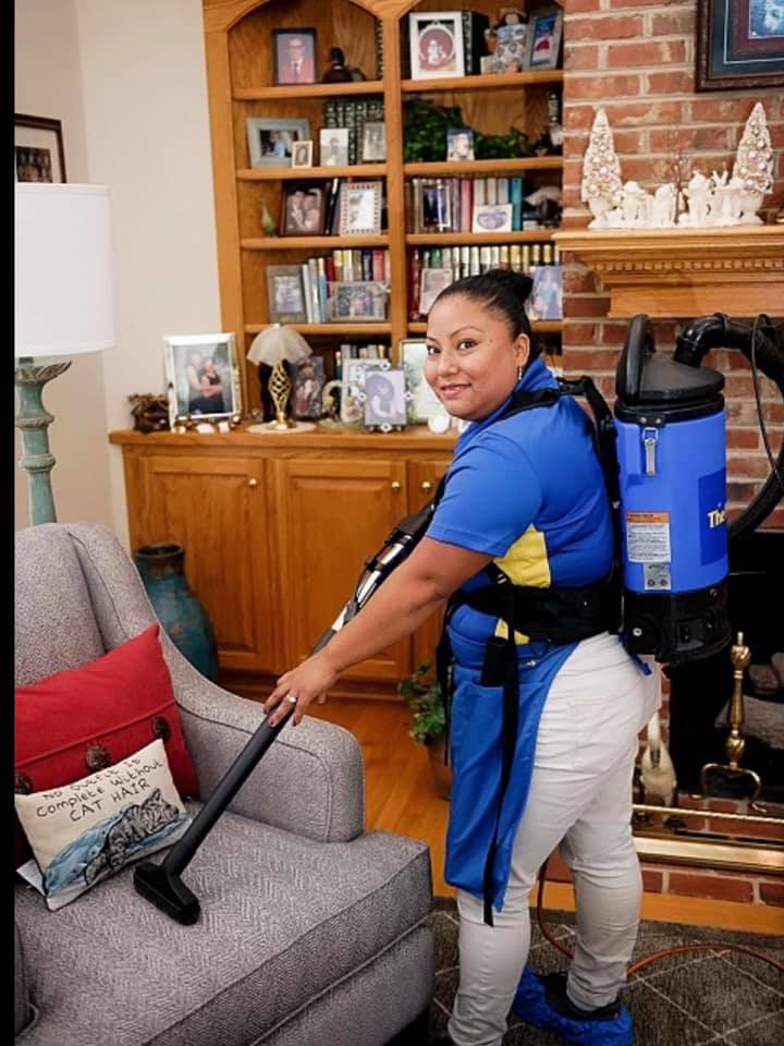A professional cleaner from Five Star Elite Maid Services vacuuming an armchair in a living room in Shreveport, LA