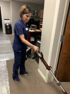 A professional cleaner in blue scrubs vacuuming a carpeted hallway, showcasing cleaning services by Precise Cleaning Solutions in Auburn, AL.