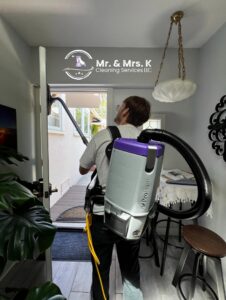 A professional cleaner from Mr. & Mrs. K Cleaning Services LLC using a backpack vacuum to clean a doorway in Sacramento, CA.