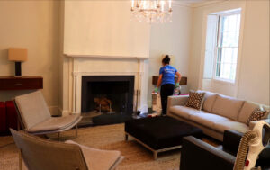 A house cleaner from Supreme Home Cleaning, Inc vacuuming a spacious living room with a fireplace in Boston, MA.