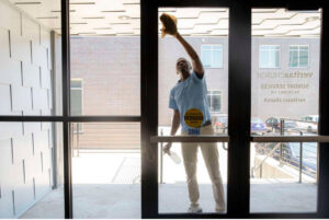 A cleaner from MJ Commercial & Residential Cleaning, LLC washing a glass door with spray and cloth in Cedar Rapids, IA.