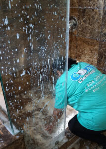A professional cleaner from Cozy Cleaning VA washing a soapy glass shower door in a client's bathroom in Richmond, VA.