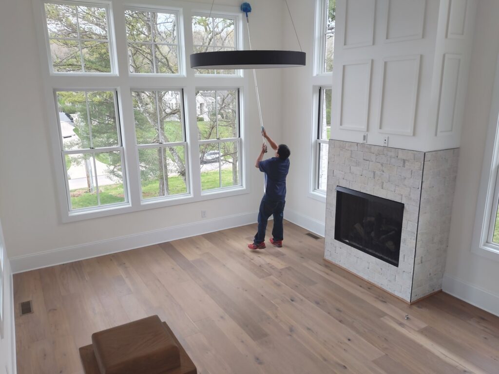 A professional cleaner from Absolute Luxury, LLC Residential & Commercial Cleaning washes high windows in a spacious living room in Antioch, TN.