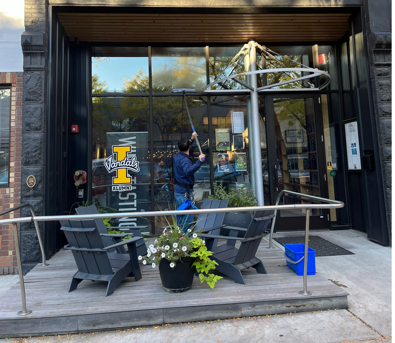 A professional cleaner washing a large storefront window with a squeegee for Gavin's Cutting Edge in Moscow, ID.