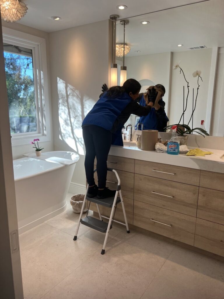 A cleaner from Fabylous Cleaning Service wiping a large bathroom mirror in Anaheim, CA.