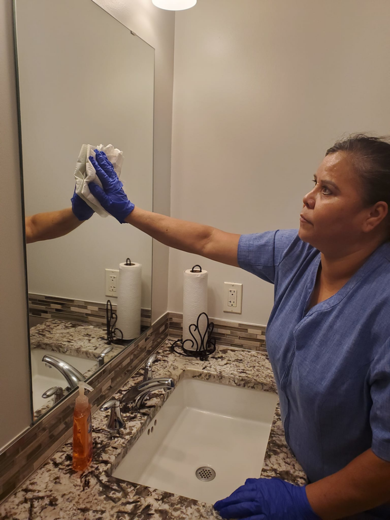 A professional cleaner from JCS Cleaning Service in Tulsa, OK, meticulously wiping a bathroom mirror.