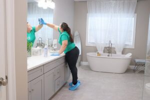 A house cleaner from Supreme Home Cleaning, Inc wiping a bathroom mirror, wearing protective shoe covers in Boston, MA.