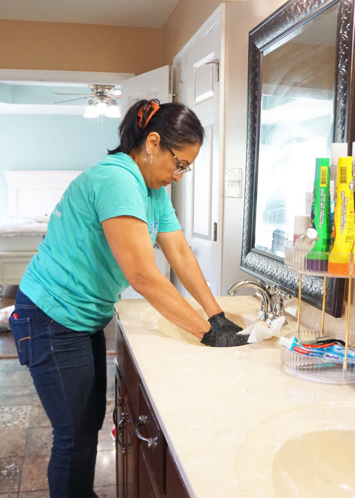 A professional cleaner from Cozy Cleaning VA wiping down a bathroom sink and countertop in a home in Richmond, VA.